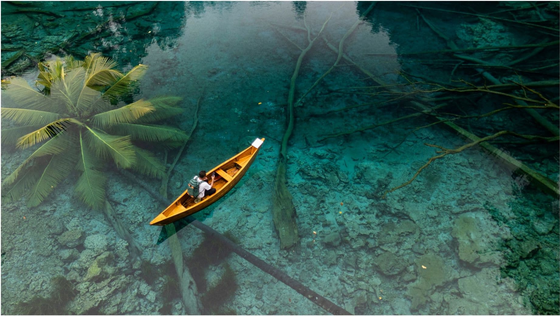 A person paddling a wooden canoe on glassy turquoise water with a Starlink Mini visible aboard.