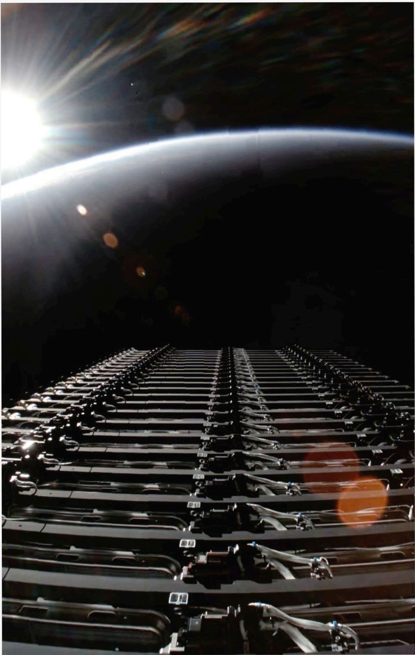 A row of Starlink satellites in deployment formation, sun rising at horizon over Earth's atmosphere.